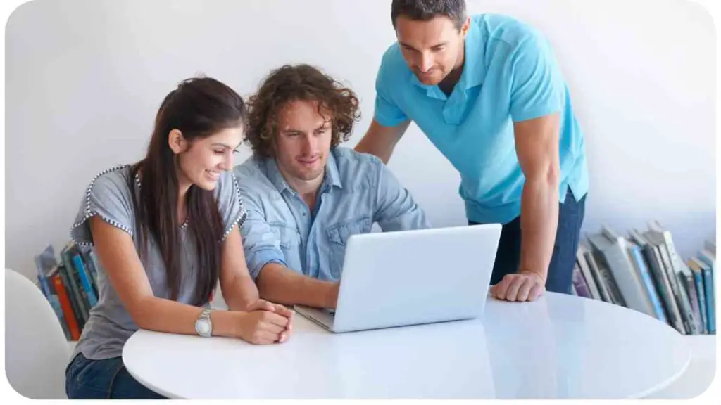 three people sitting around a table looking at a laptop